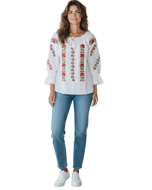 Woman wearing a white blouse with red floral embroidery and blue jeans on a white background