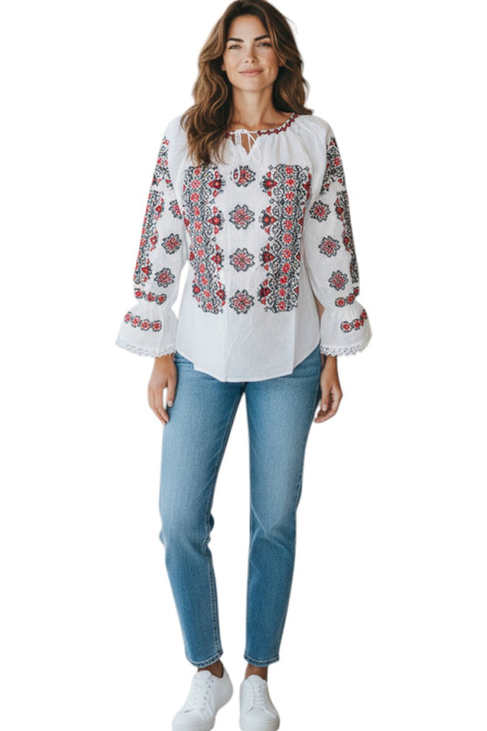 Woman wearing a white blouse with red floral embroidery and blue jeans on a white background