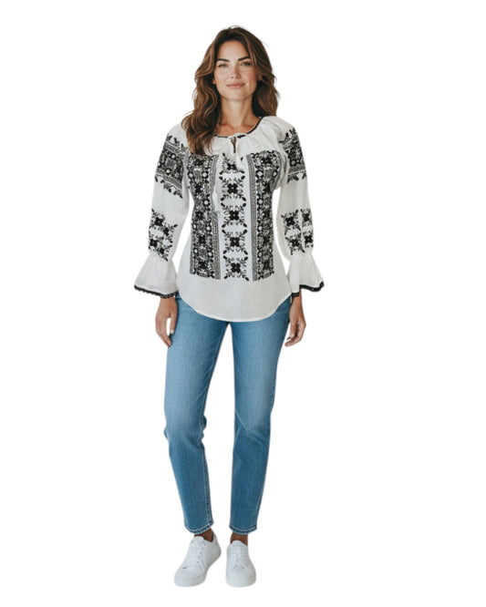 Woman wearing a white blouse with black embroidery and blue jeans on a white background
