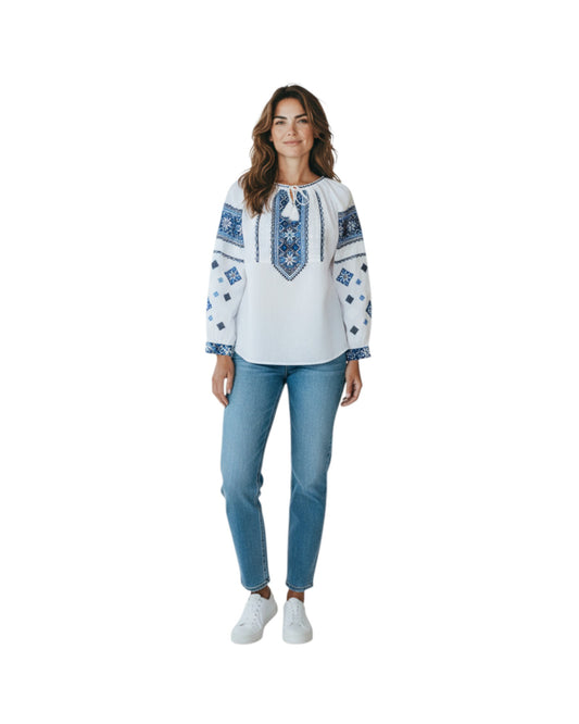 Woman wearing a white blouse with blue embroidery and light blue jeans on a white background
