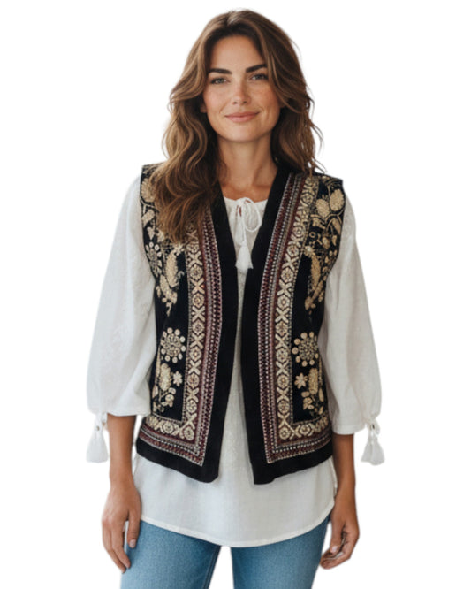 Woman wearing a black embroidered vest over a white blouse on a white background